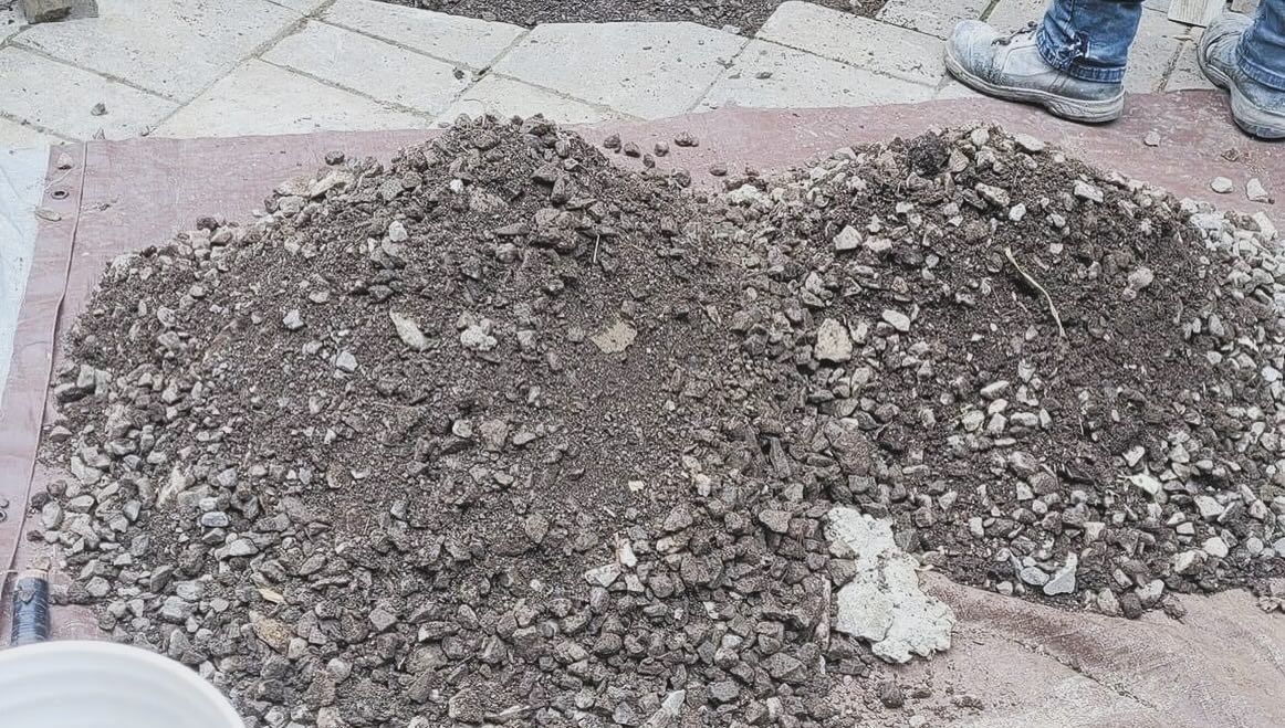 Pile de matériaux sombres et cassés sur un drap rose, les pieds d'une personne en arrière-plan.