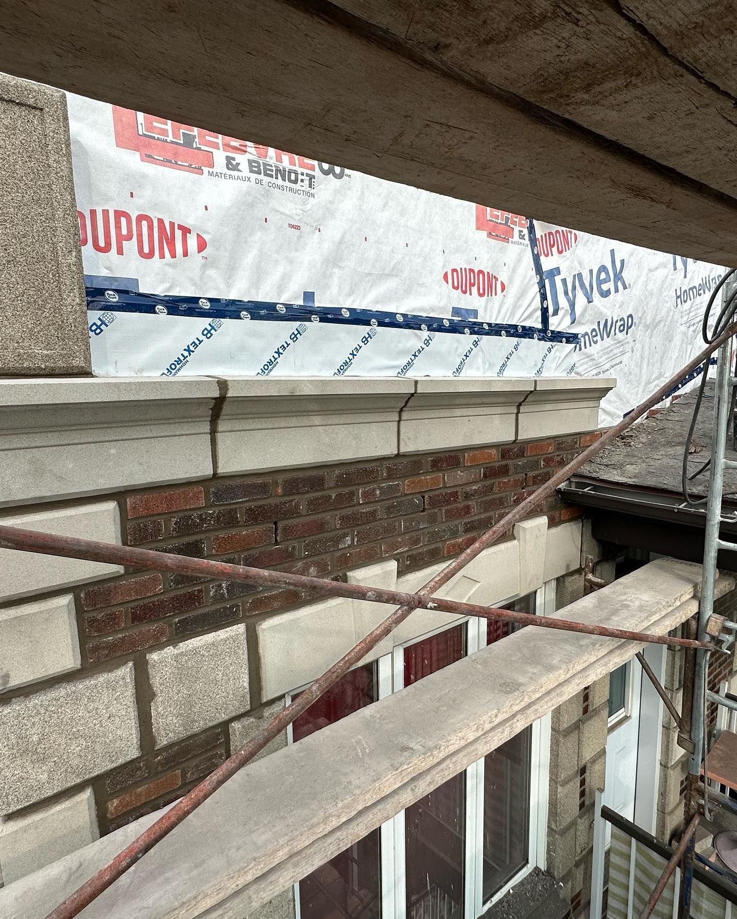 Construction des murs extérieurs : briques rouges et pierres grises avec pare-intempéries Dupont Tyvek visible. Échafaudage présent.