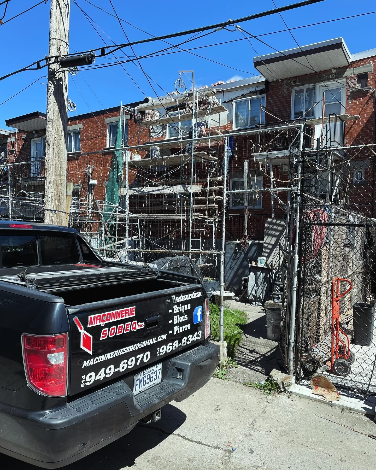 Camion noir garé devant un bâtiment en construction avec échafaudage. Ciel bleu au-dessus.