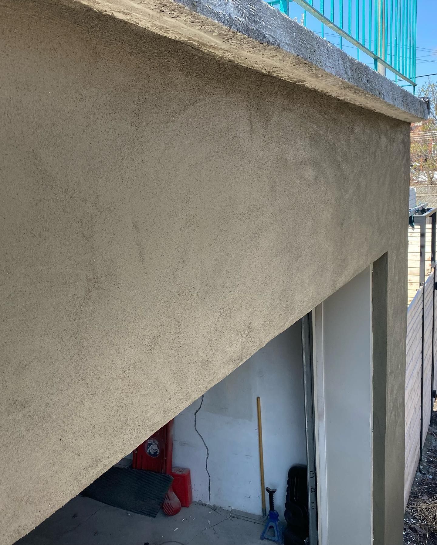 Extérieur d'un bâtiment avec des murs en stuc, un garage partiellement ouvert et une balustrade bleue au-dessus.