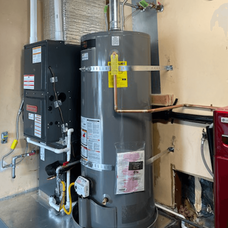 A furnace and water heater installed in a room with a damaged wall.