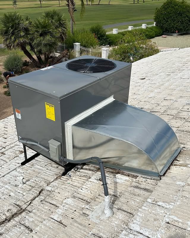 Rooftop HVAC unit, gray and silver, on a light-colored tile roof with greenery and a golf course in the background.
