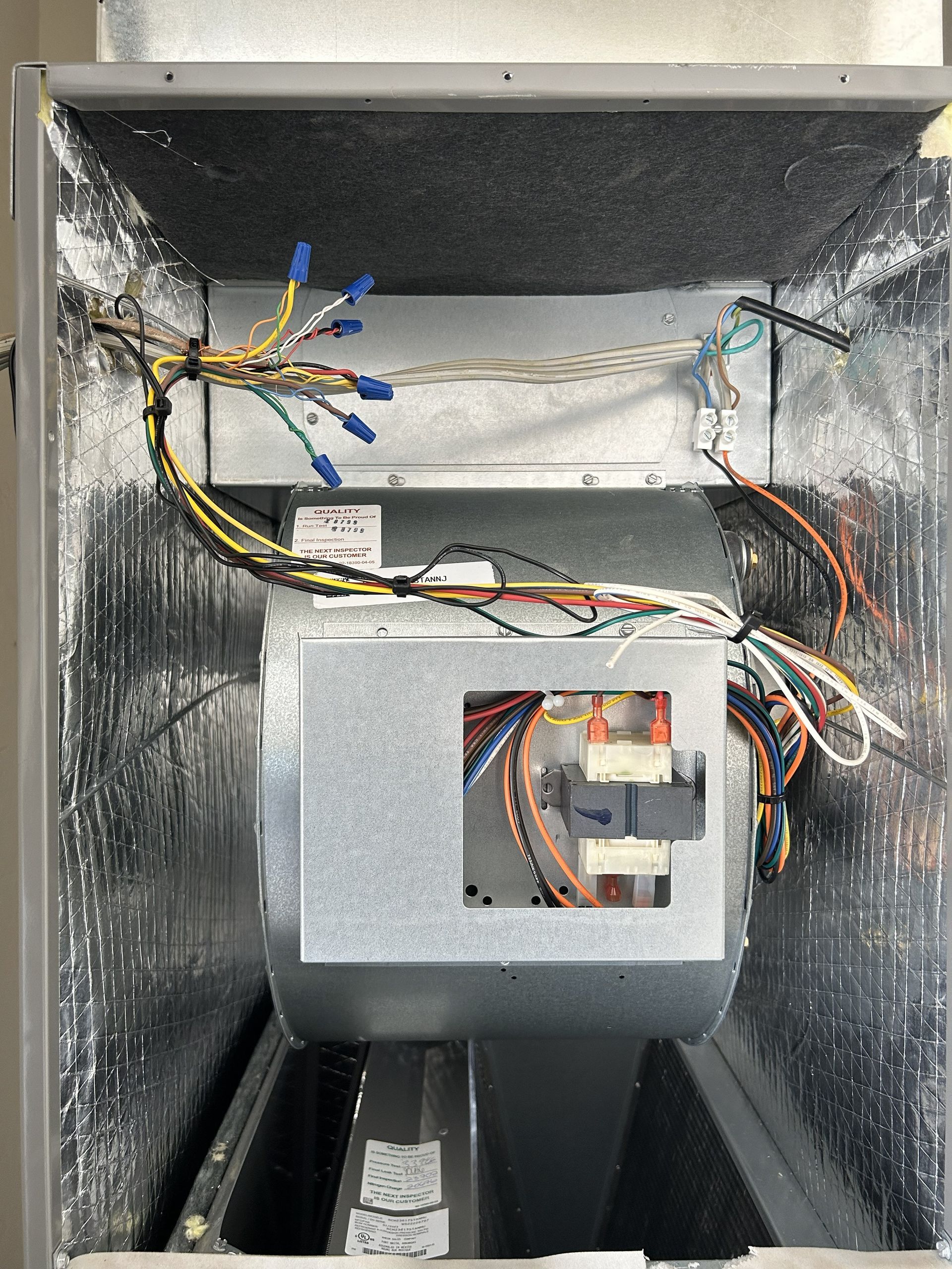 Interior view of an air handler unit with wiring and a control panel. Silver insulation lines the metal casing.