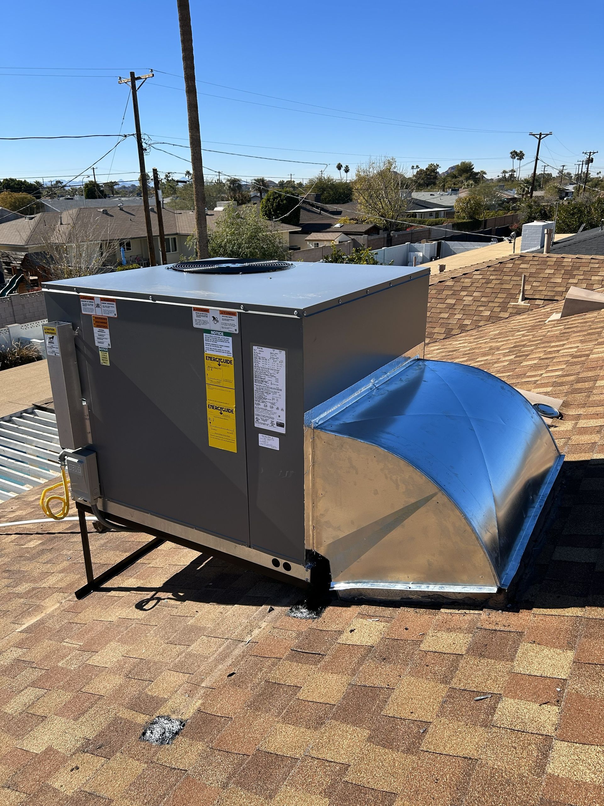 Rooftop HVAC unit, gray and silver, on a tiled roof under a blue sky.