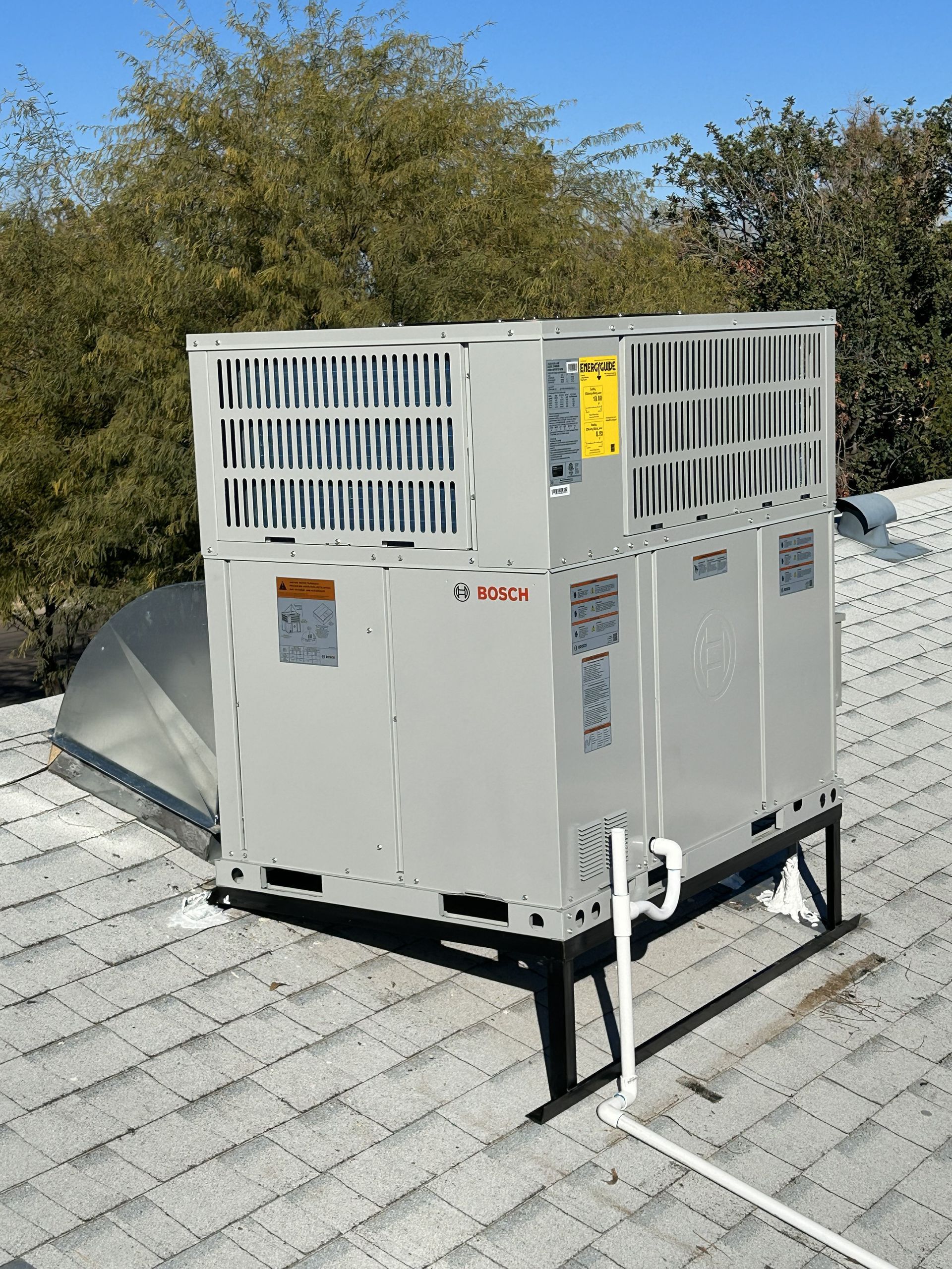 Rooftop air conditioning unit on a shingled roof, with white and gray metal components.