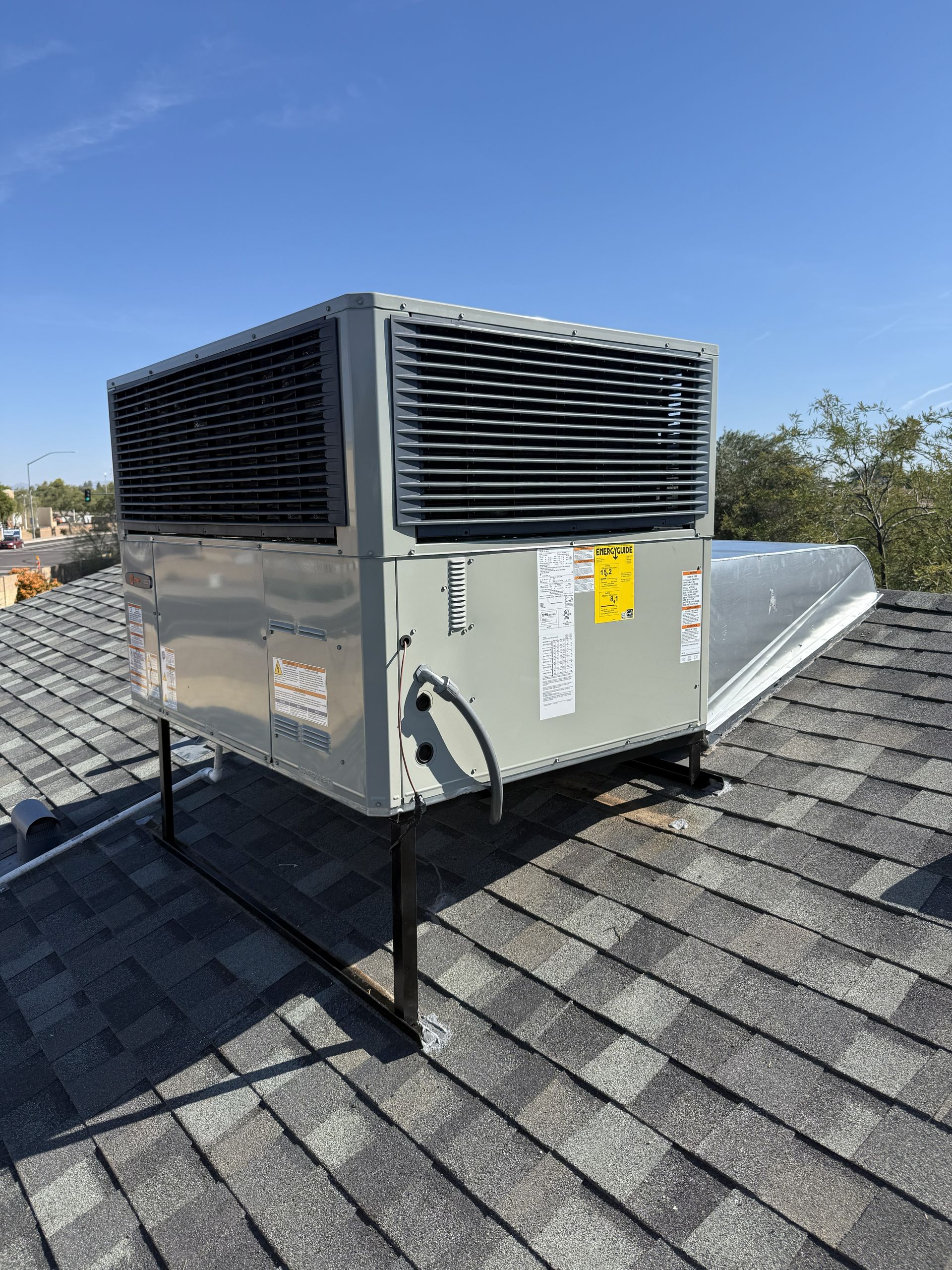 Rooftop HVAC unit on a shingled roof under a clear blue sky.