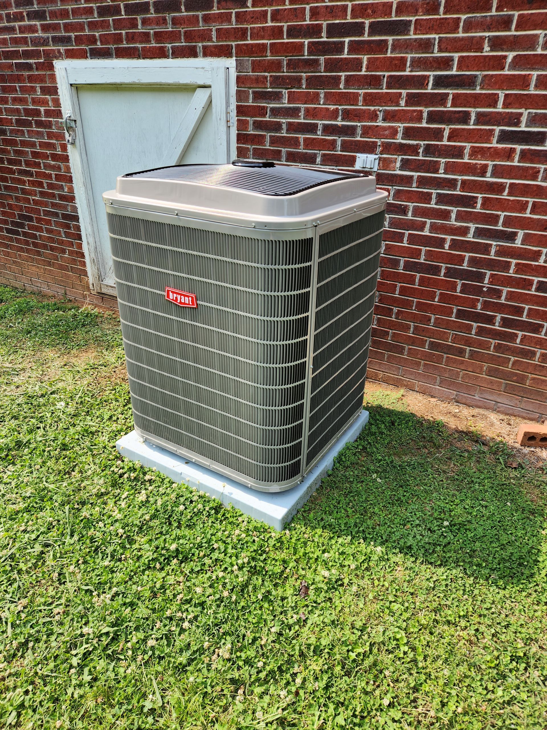 Air conditioner unit on a concrete pad outside a brick building, green grass in front.