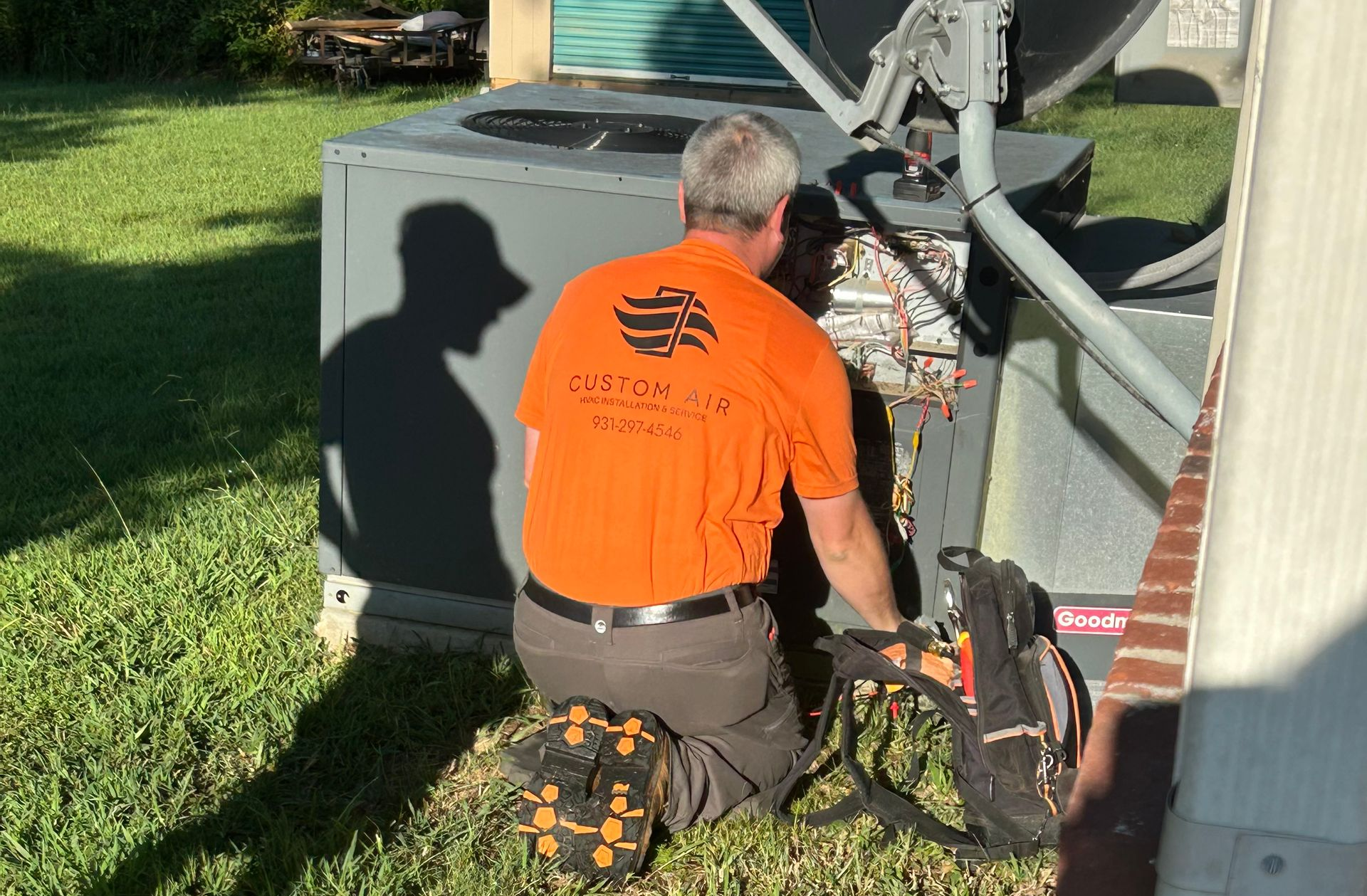 HVAC technician kneeling, working on an air conditioning unit outdoors on a sunny day.