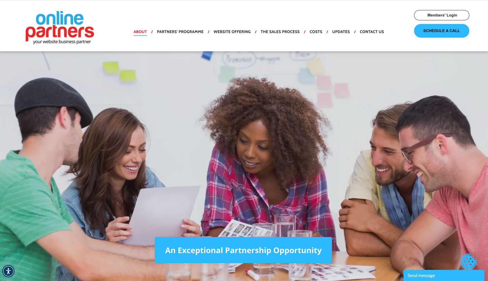 Group of people looking at a laptop, cheerful expressions, in front of a white board.