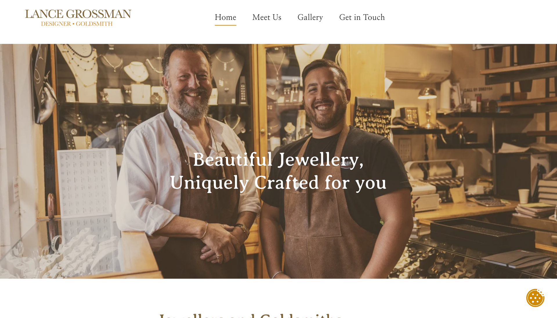 Two smiling jewelers in workshop setting, with jewelry display. 