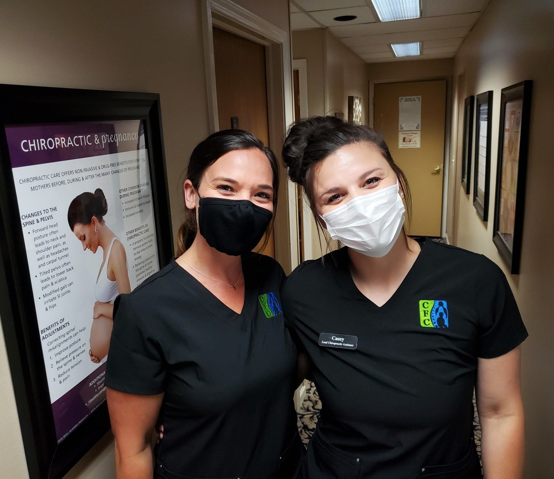 Two women wearing masks are posing for a picture in a hallway