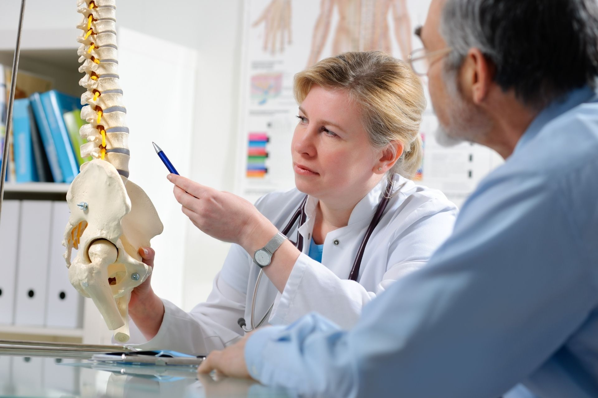 A doctor is talking to a patient while holding a model of a spine.