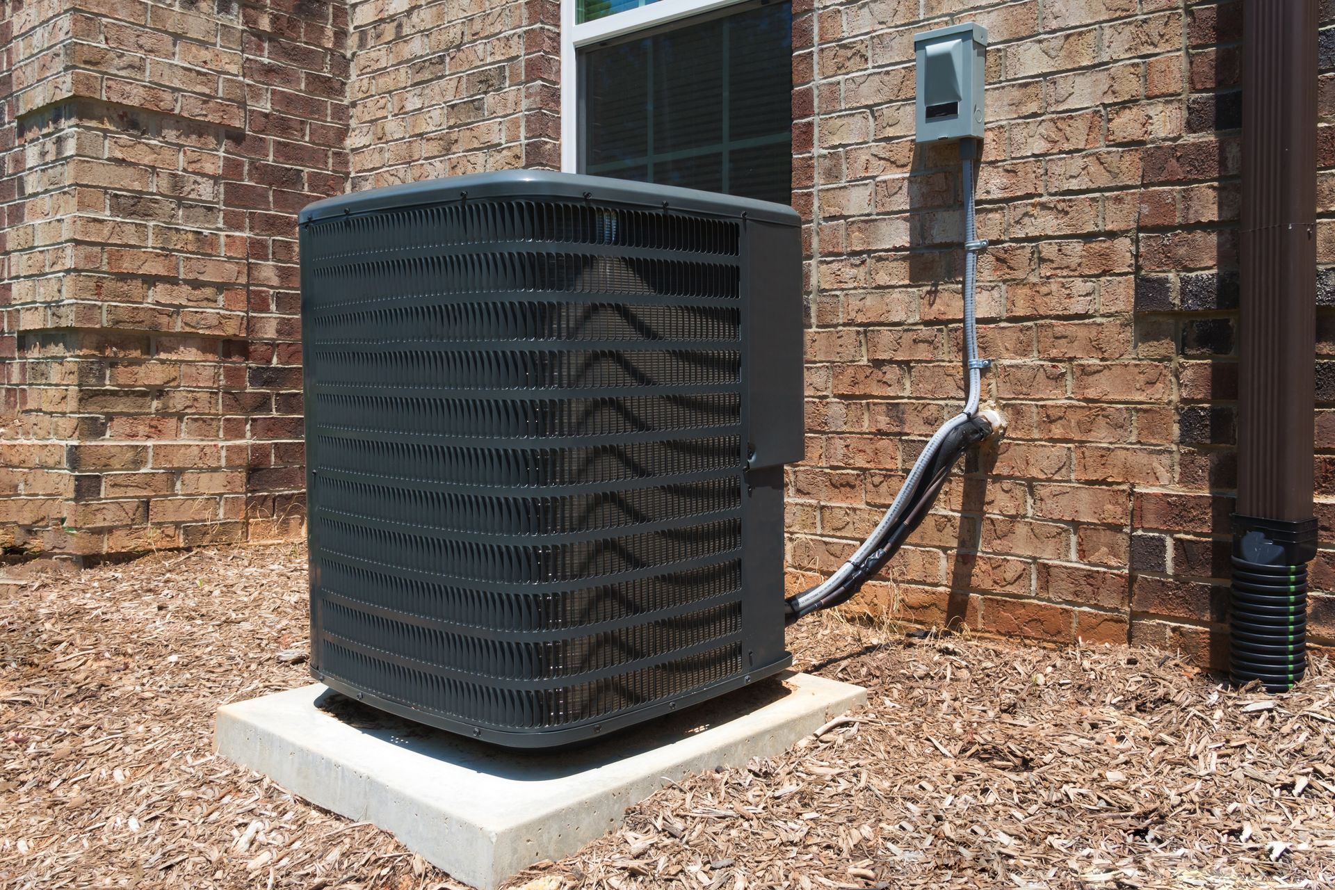 A black air conditioner is sitting outside of a brick building.