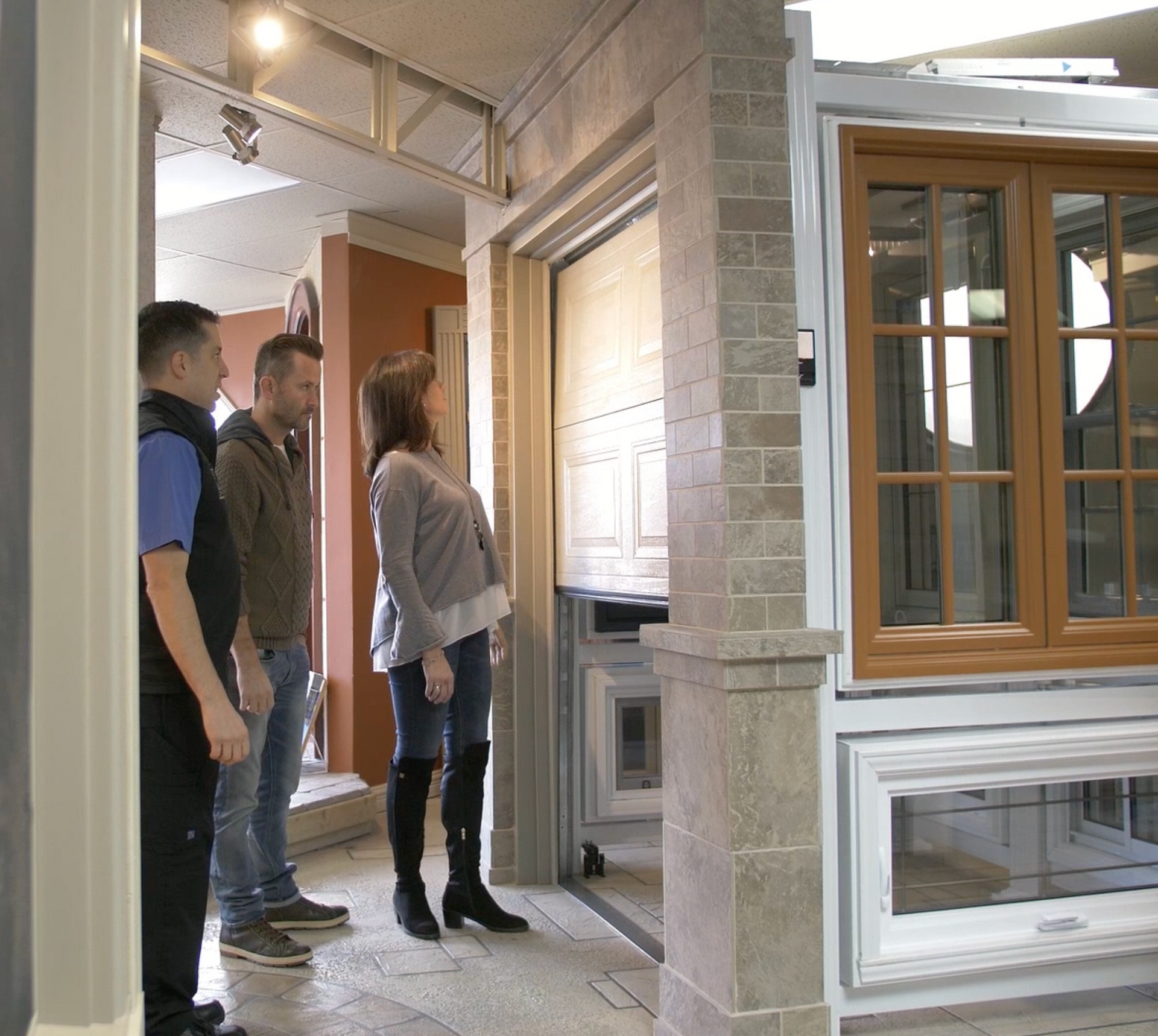 Trois personnes observent une porte de garage exposée dans une salle d'exposition.