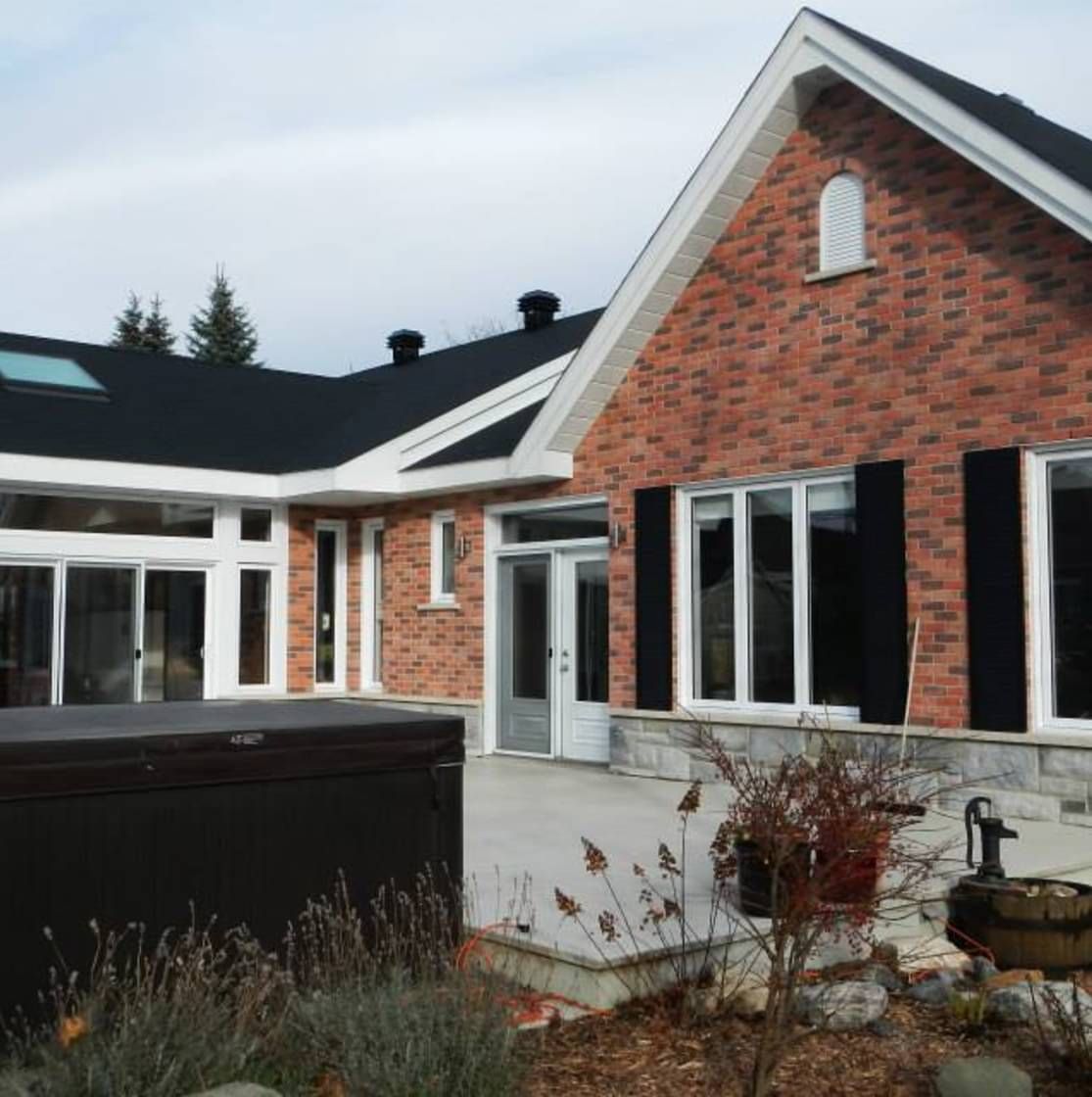 Une maison en briques avec un toit noir et des volets noirs