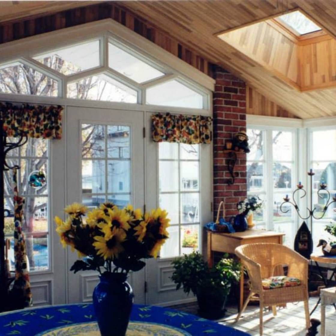 Un vase de tournesols est posé sur une table dans une pièce avec beaucoup de fenêtres