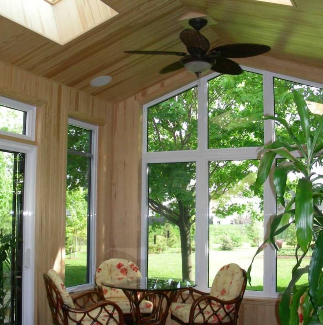 Une pièce avec un ventilateur de plafond et beaucoup de fenêtres