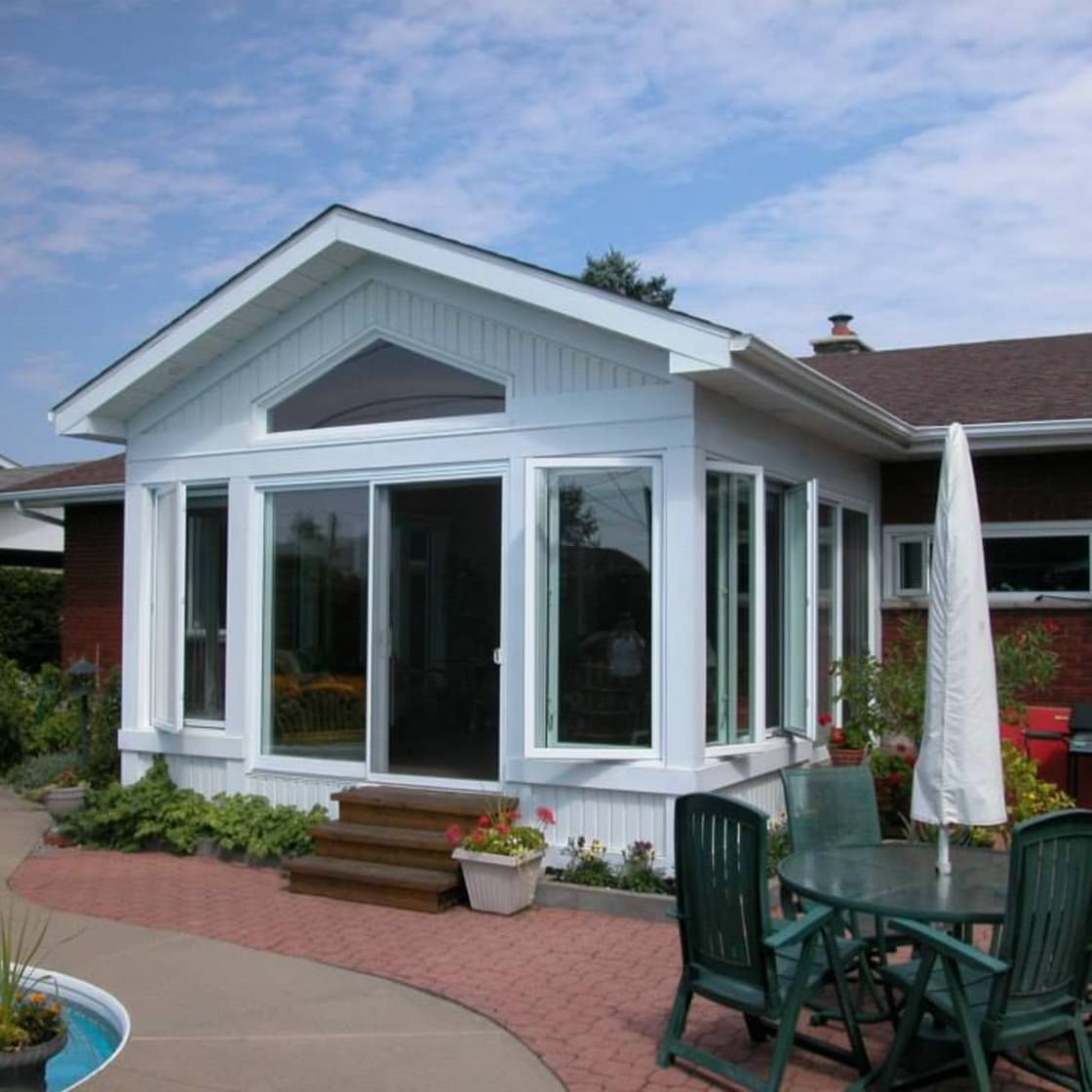 Ajout d'une véranda blanche avec fenêtres en verre et patio en briques.
