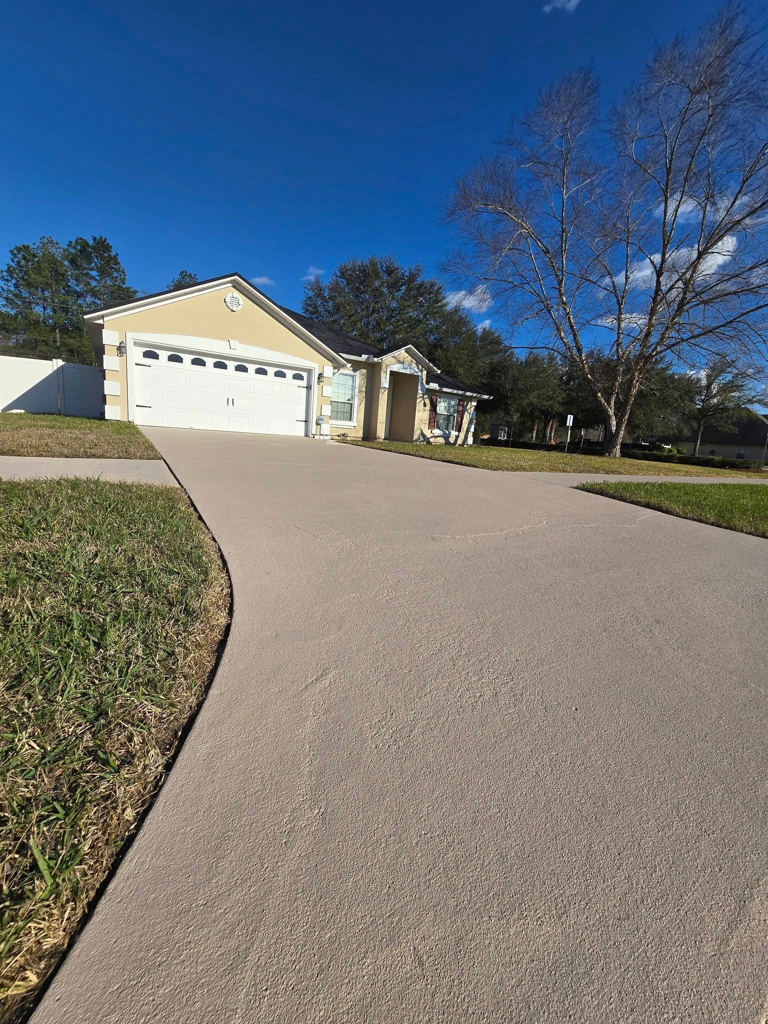 Driveway leading to a beige house with a closed garage door under a bright blue sky.