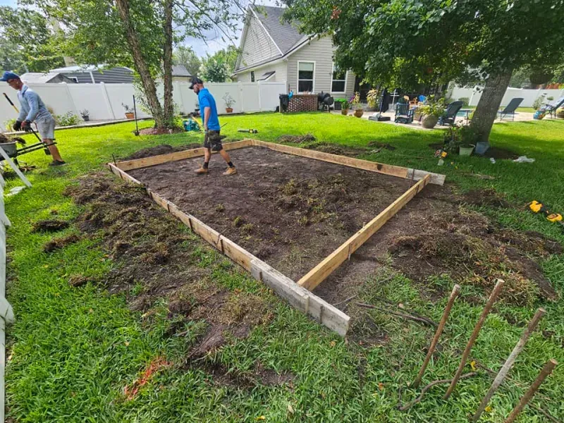 Two men building a rectangular garden bed in a grassy backyard.