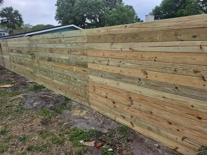 Wooden fence in a yard, showing horizontal planks of varying colors and textures.