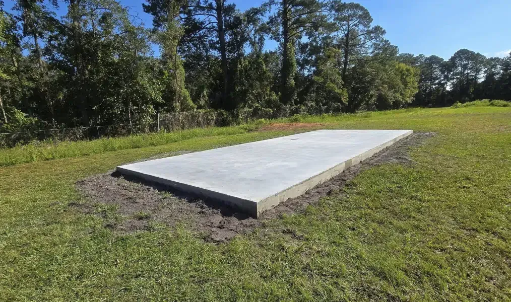 Concrete slab on grass in a grassy field with trees in the background under a blue sky.
