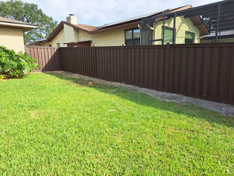 Brown fence bordering a green grassy backyard, with a house visible in the background.
