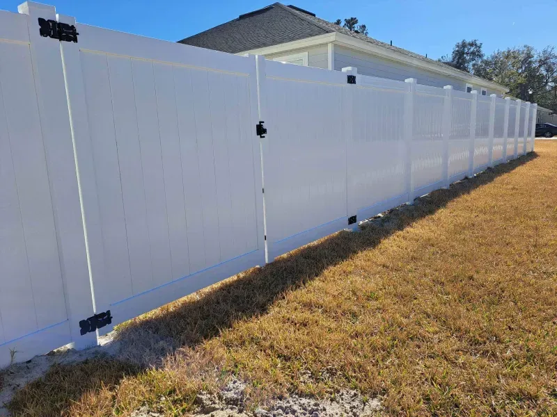 White vinyl fence enclosing a grassy yard, with a black gate and hardware.