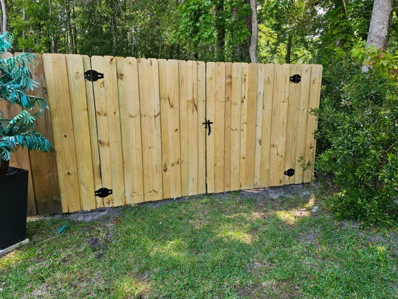 Wooden double gate with black hinges and latch, set in a grassy yard.