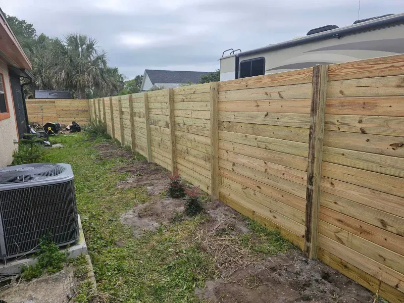 Wooden fence in a backyard, beside a house and RV, on a cloudy day.