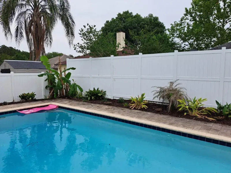 Swimming pool with white fence, landscaping, and tropical foliage.