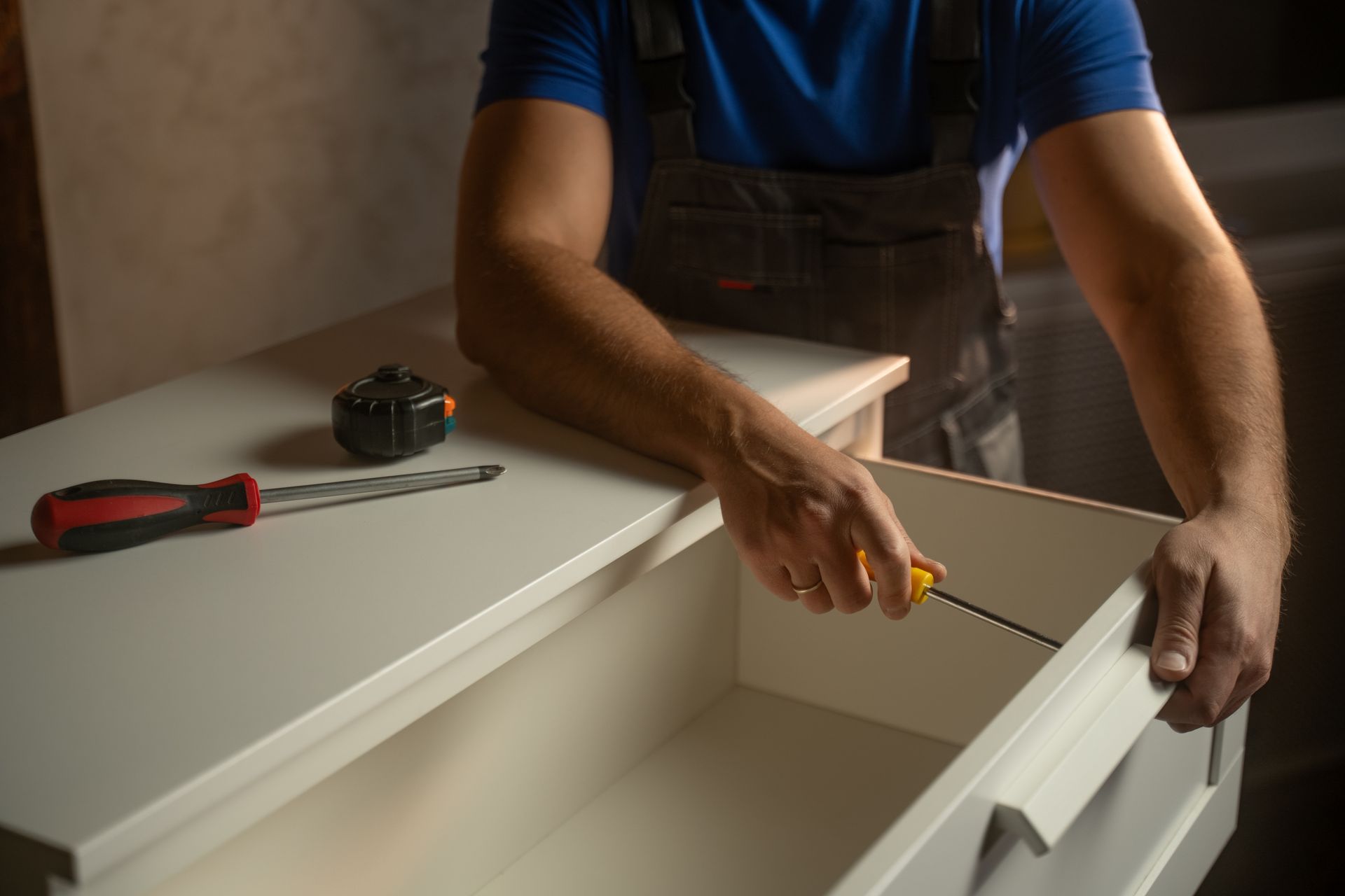 A person assembling a white dresser drawer, using a screwdriver.