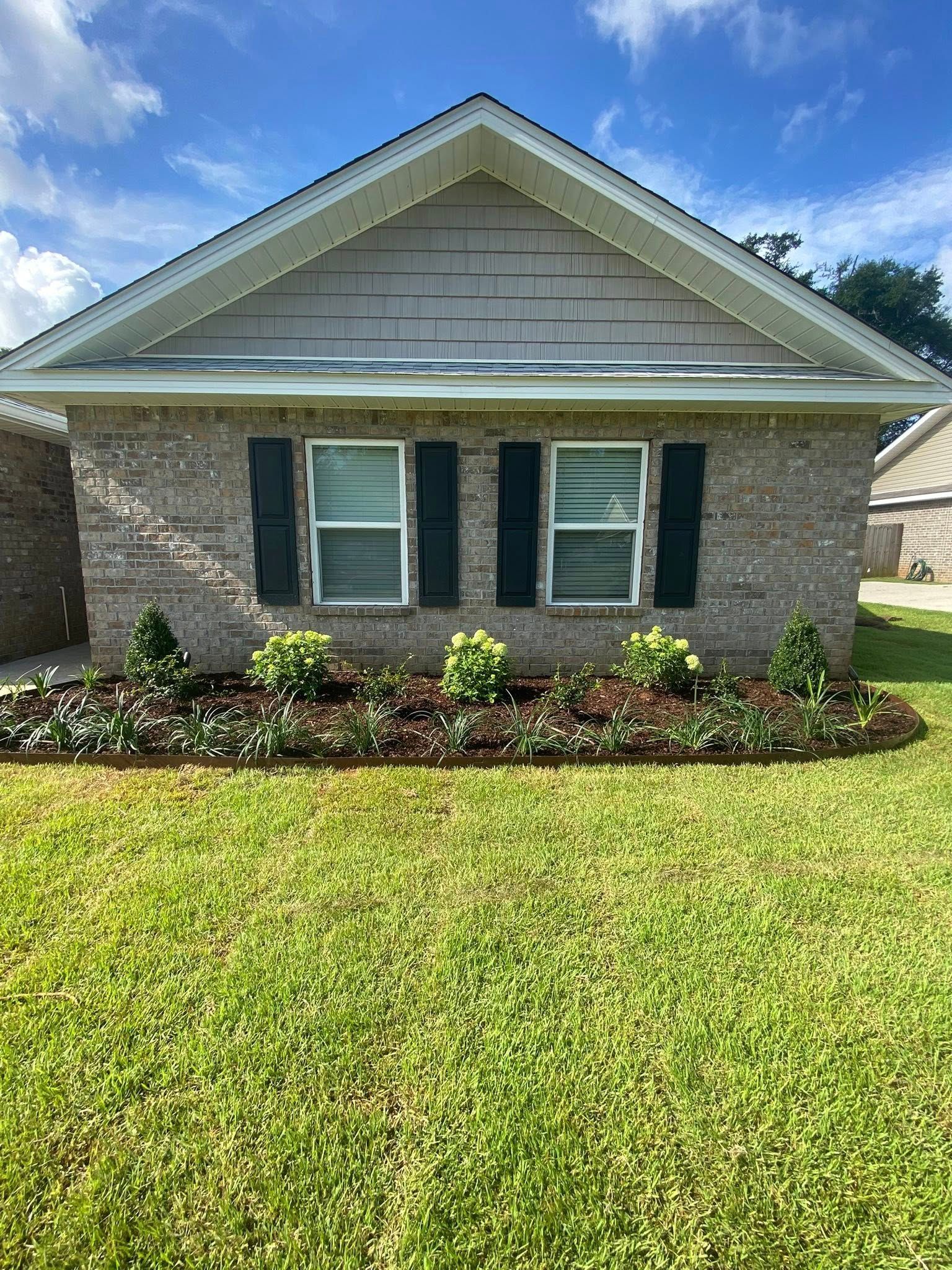 Brick house with two windows, black shutters, and a well-manicured yard under a blue sky.