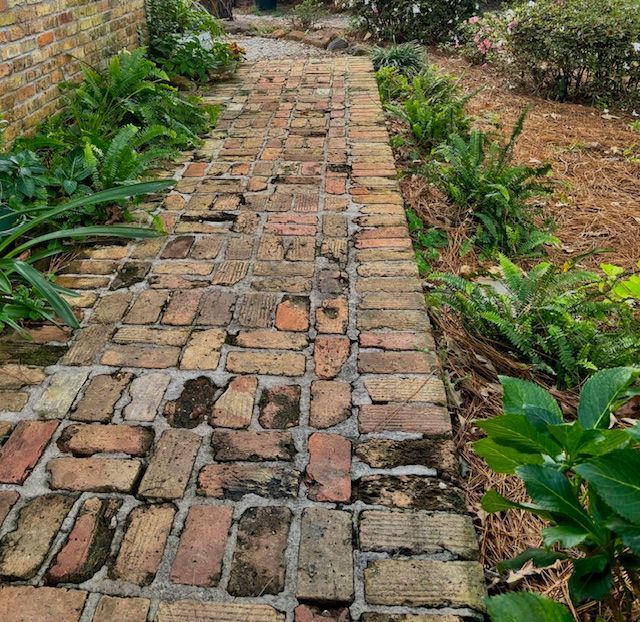 Brick pathway lined with green plants, leading through a garden.