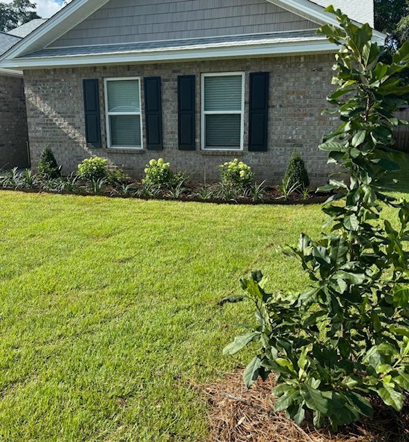 Front view of a brick house with dark shutters, a well-manicured lawn, and landscaping.