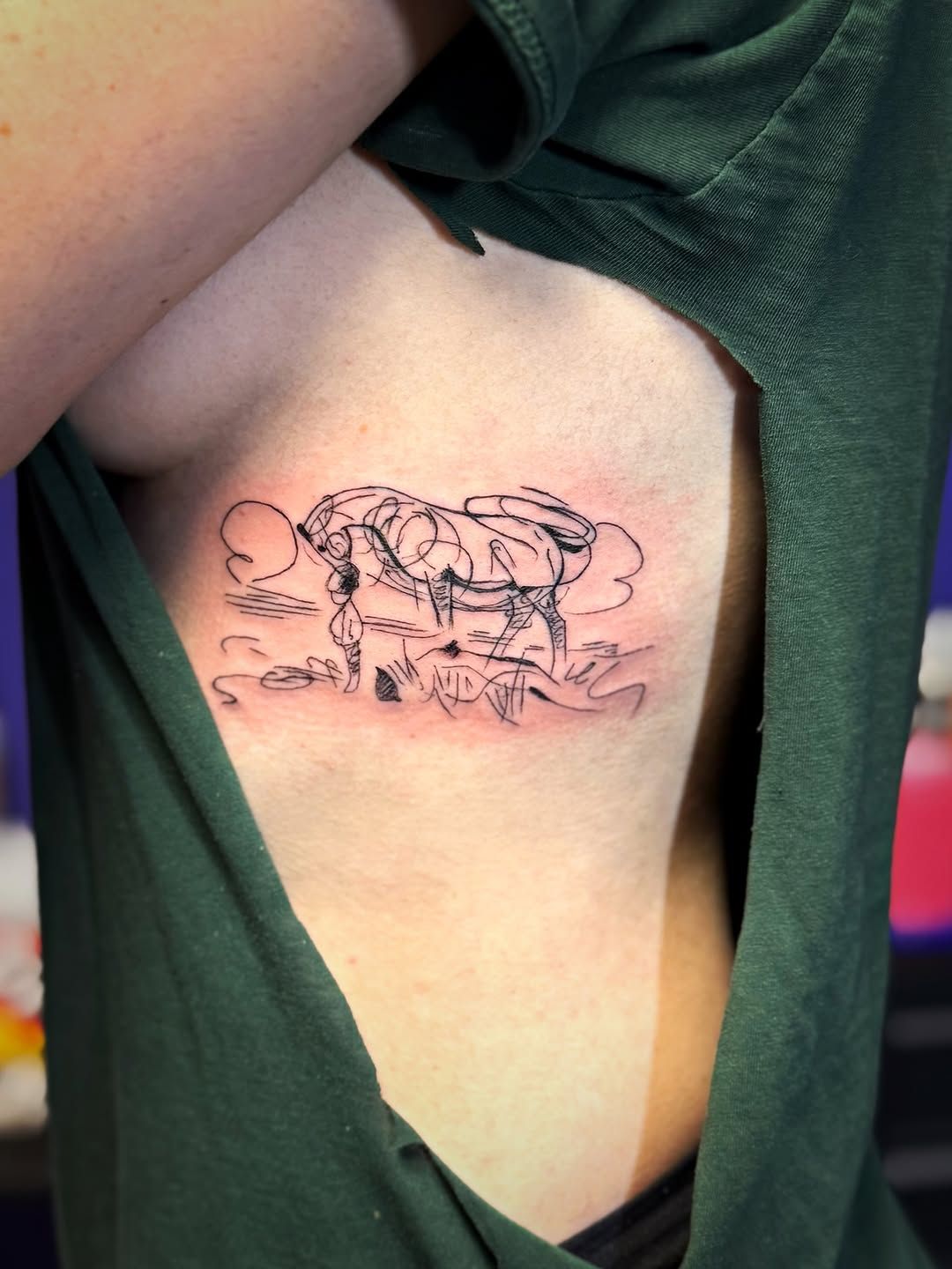 A fine-line tattoo on a person's ribcage depicting a stylized, abstract landscape with clouds, hills, and a bridge.