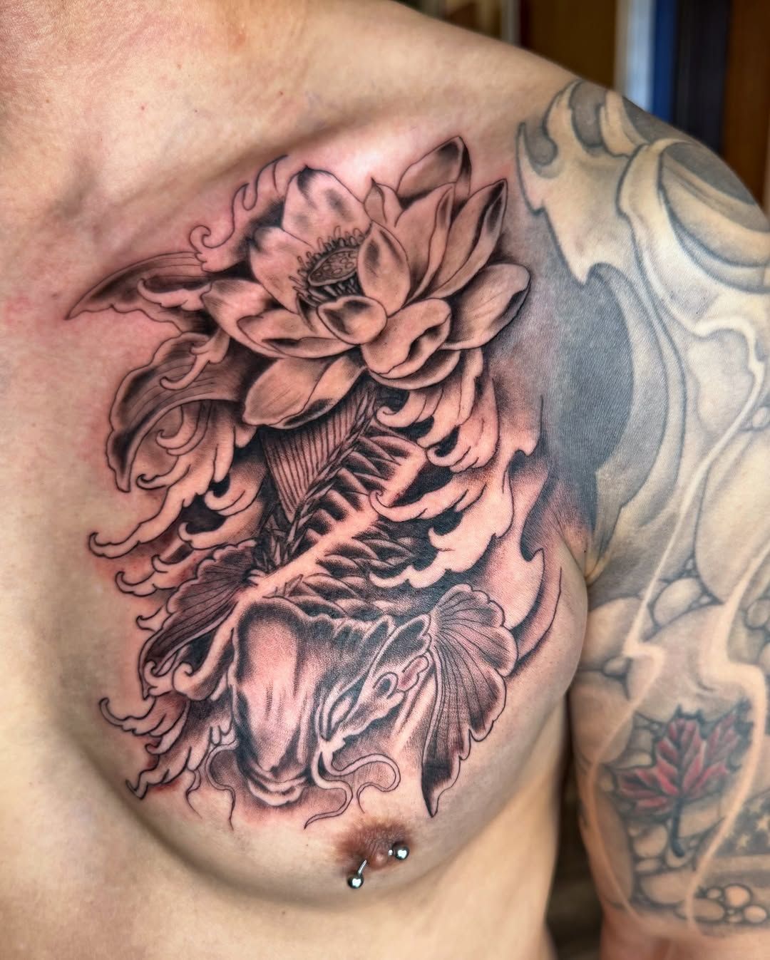 Black and grey chest tattoo featuring a koi fish swimming upward through stylized water toward a large lotus flower.