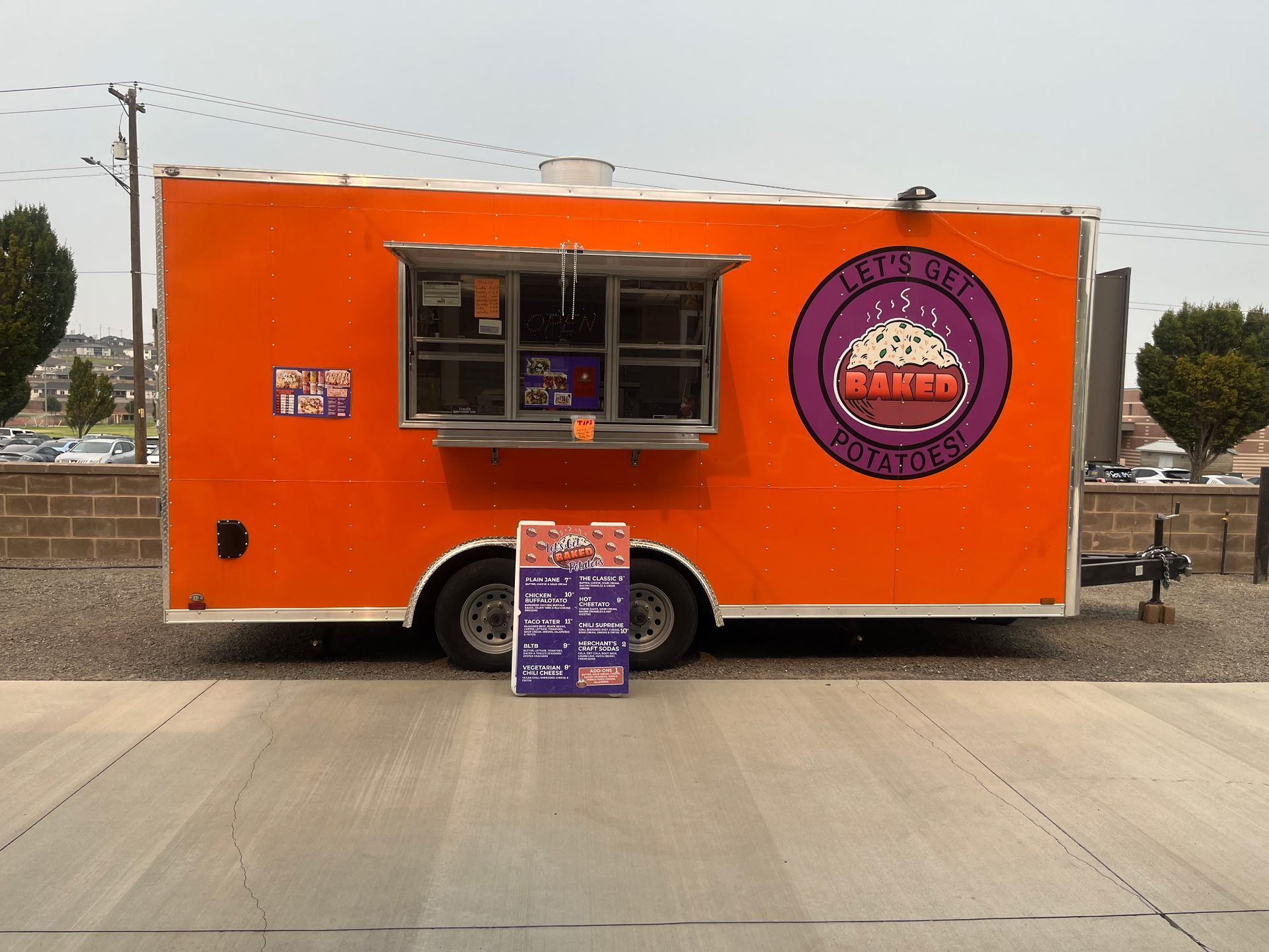 Orange food trailer with purple logo and menu sign.