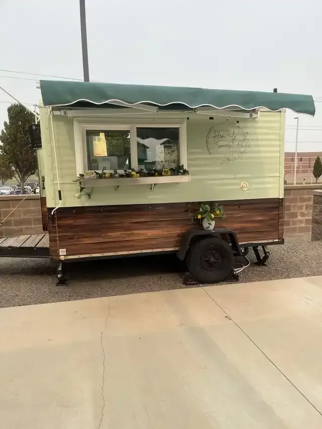 A mobile food trailer with a sage green and wood exterior, and a green awning.