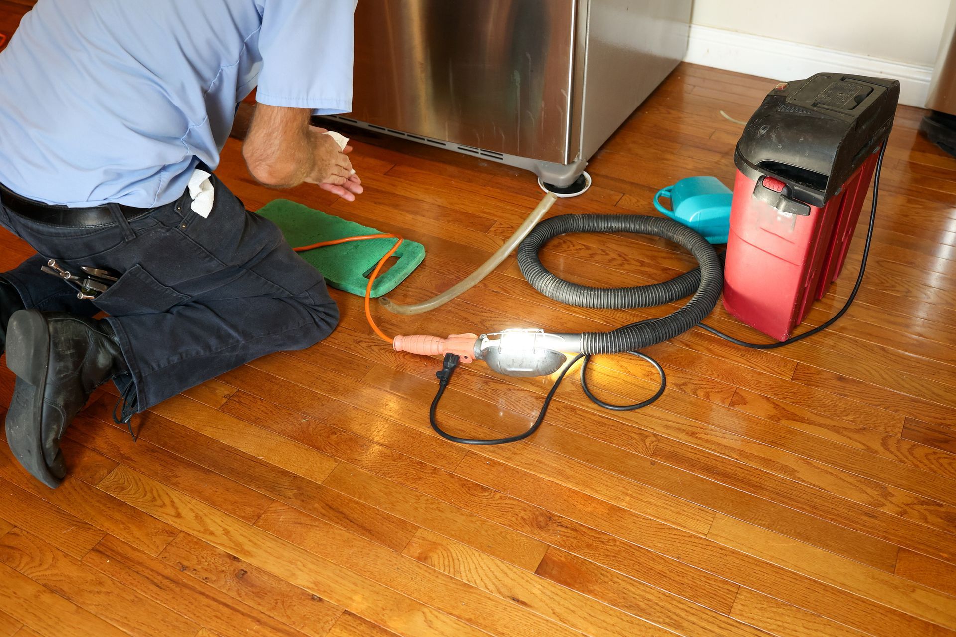 A man is kneeling on the floor next to a refrigerator.