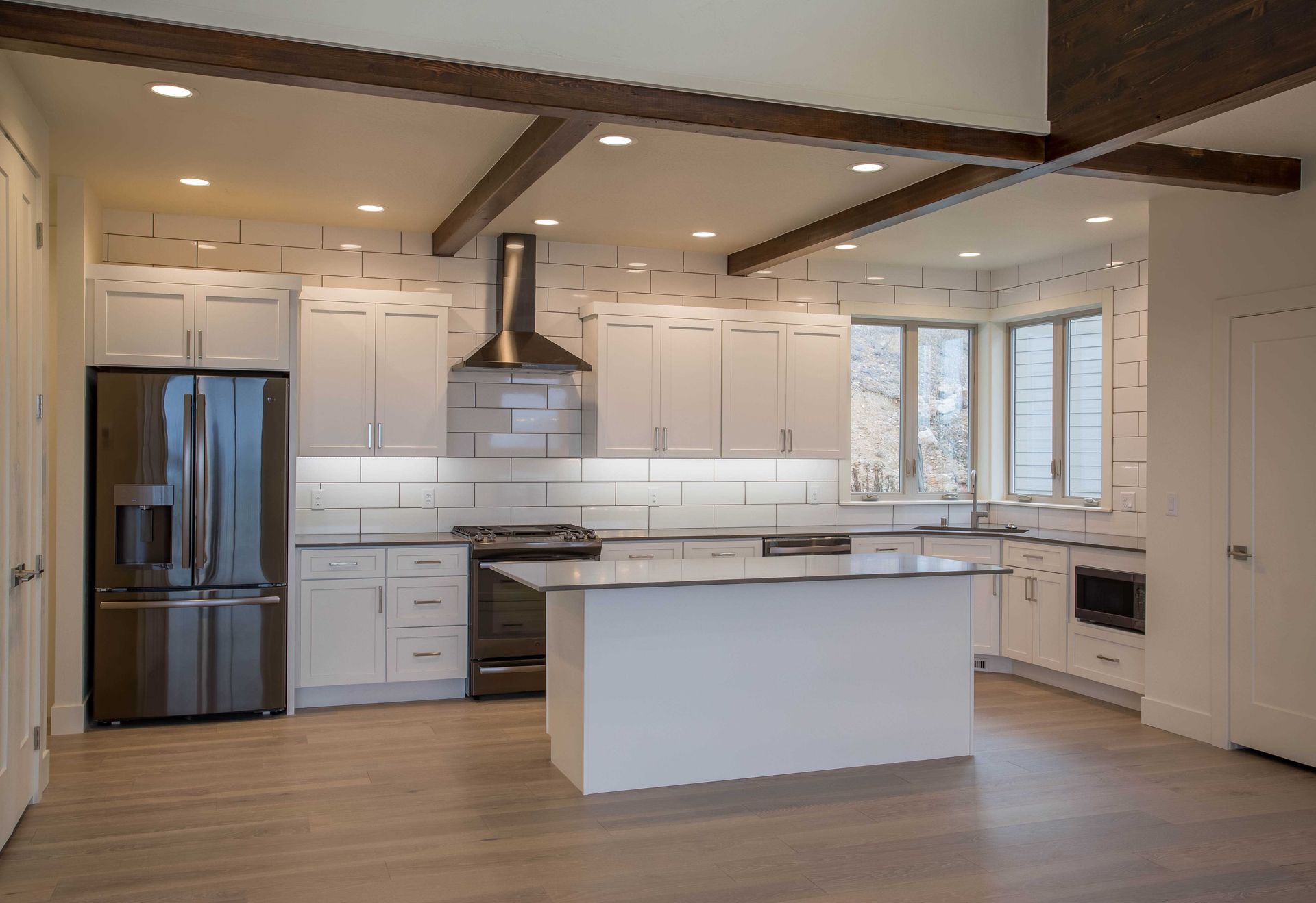 A modern kitchen featuring white cabinets, stainless steel appliances, a center island, and wood beams on the ceiling.