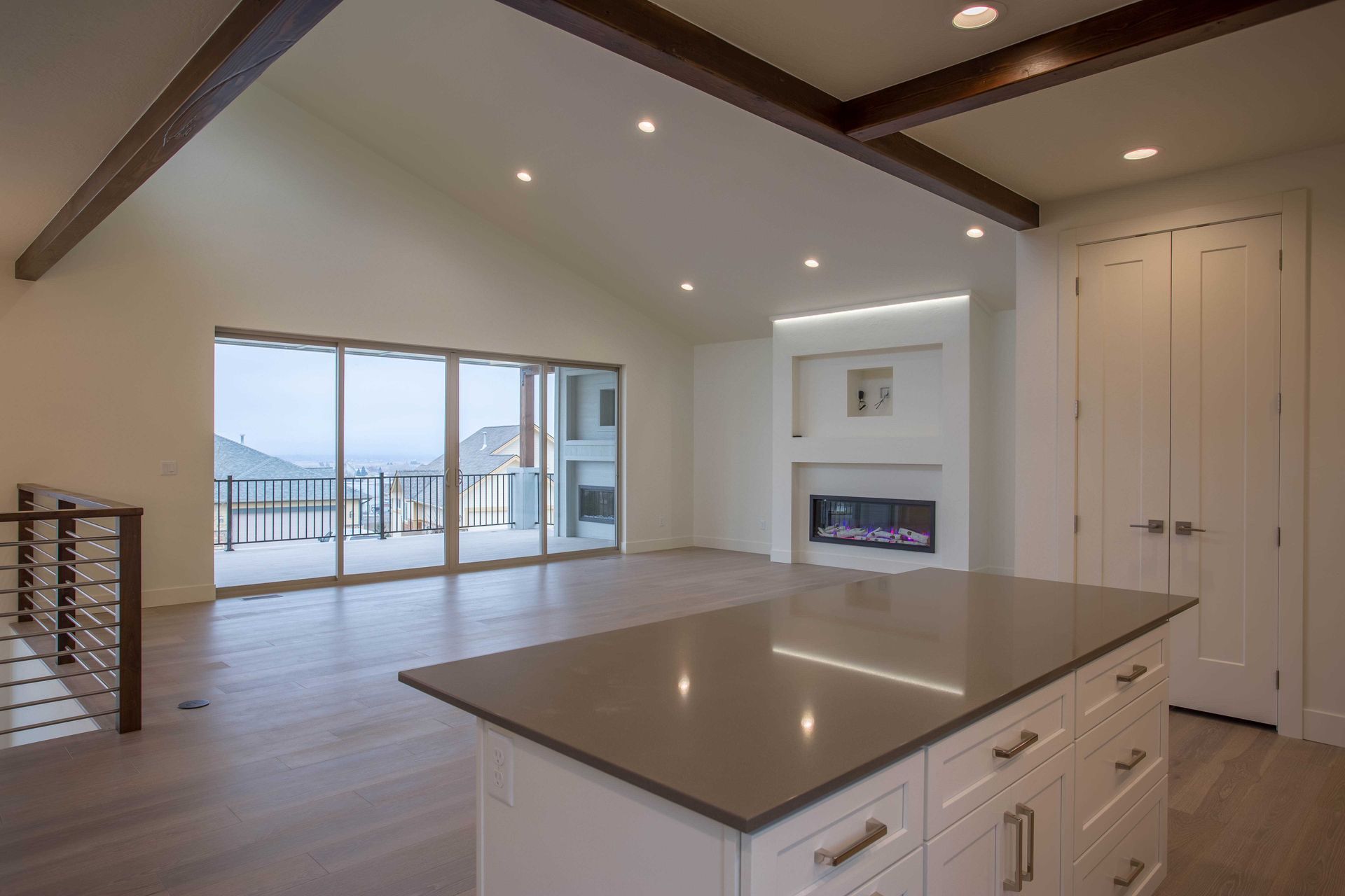 A modern, open-concept kitchen island faces a living area with a fireplace, vaulted ceiling, and sliding glass doors.