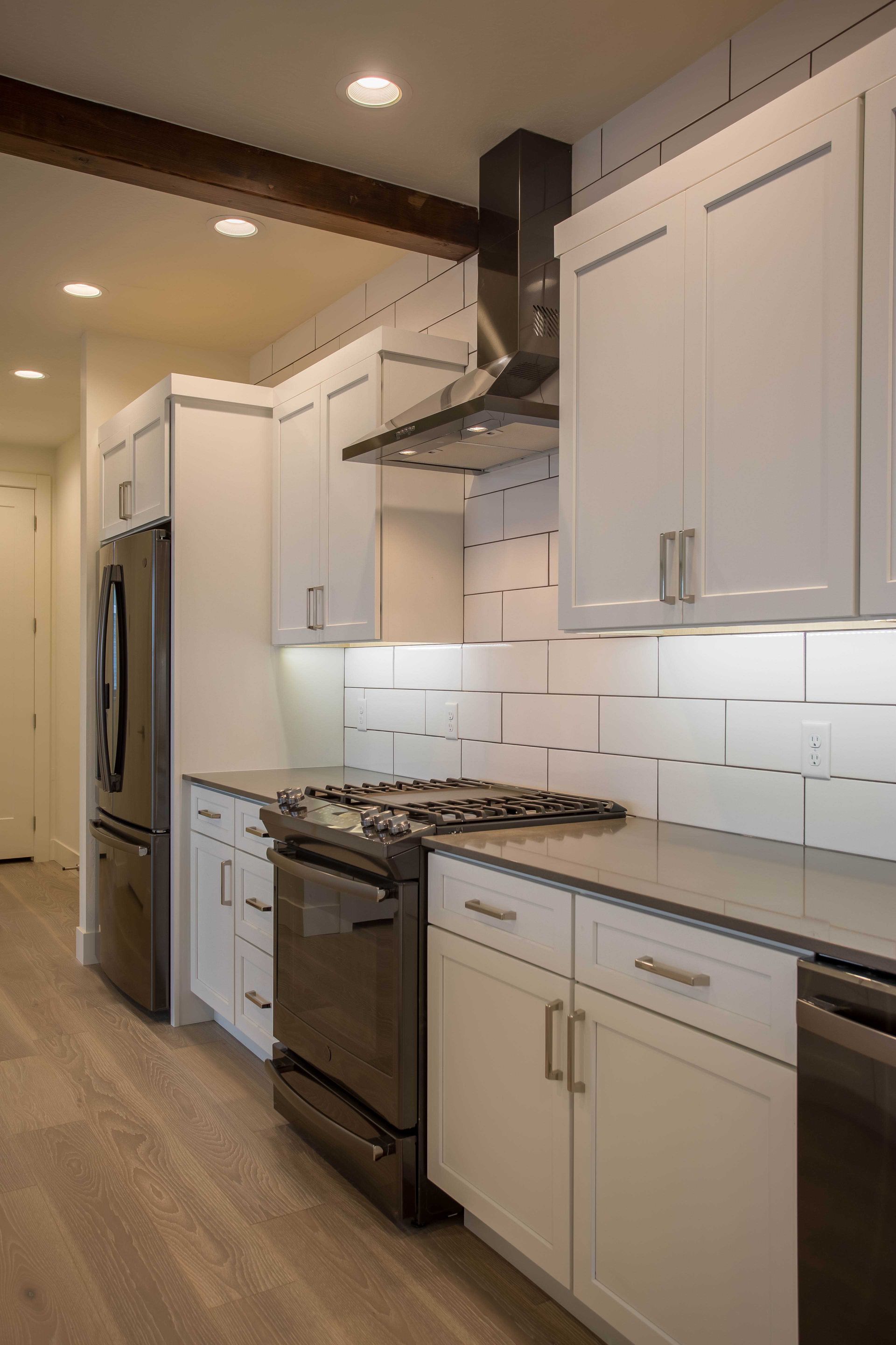 Modern kitchen with white shaker cabinets, dark appliances, a subway tile backsplash, and a wooden ceiling beam.