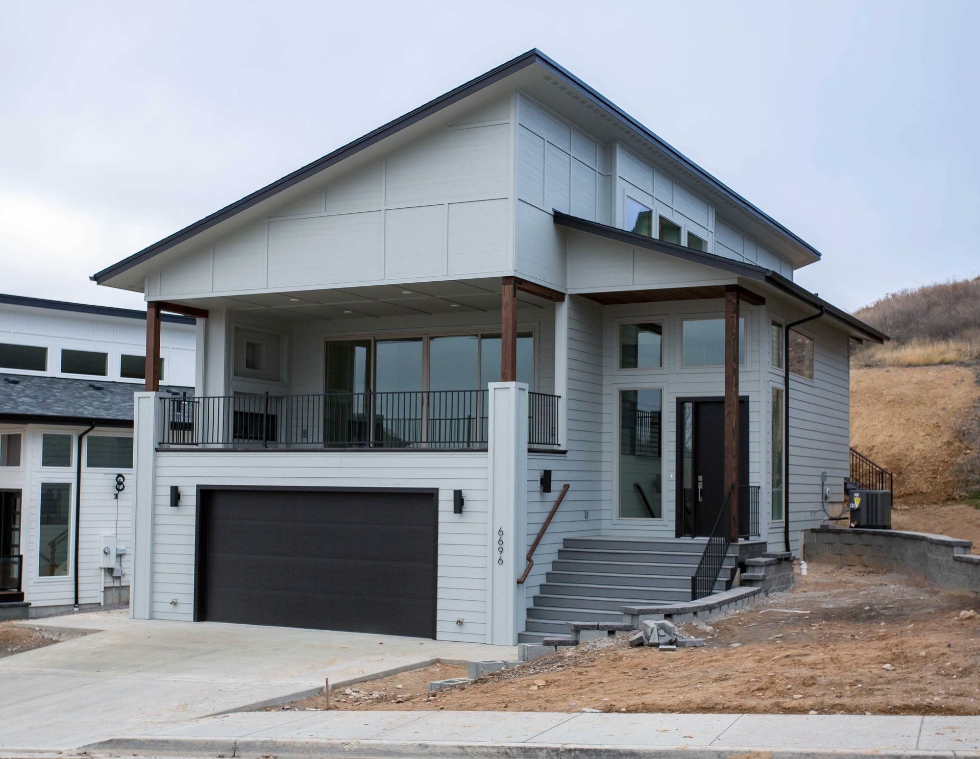 A modern two-story home with light gray siding, a dark garage door, and a raised balcony above the garage.