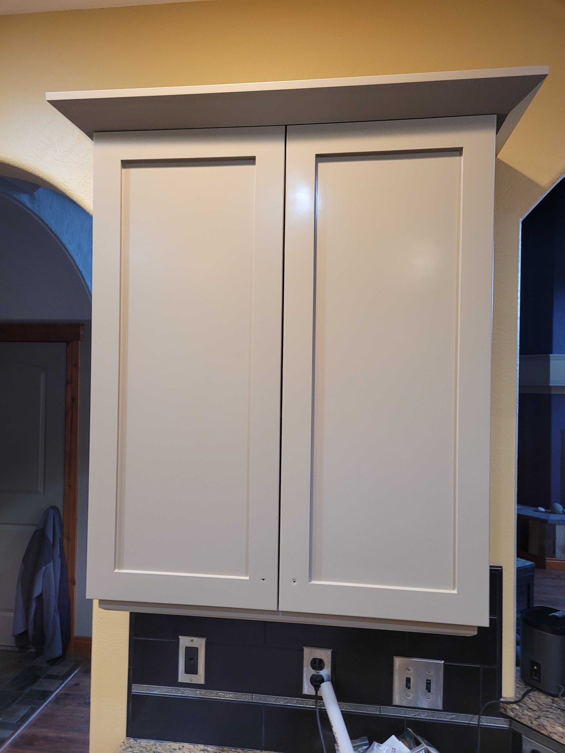 Light gray, shaker-style double kitchen cabinets mounted above a dark tiled backsplash with three wall outlets.