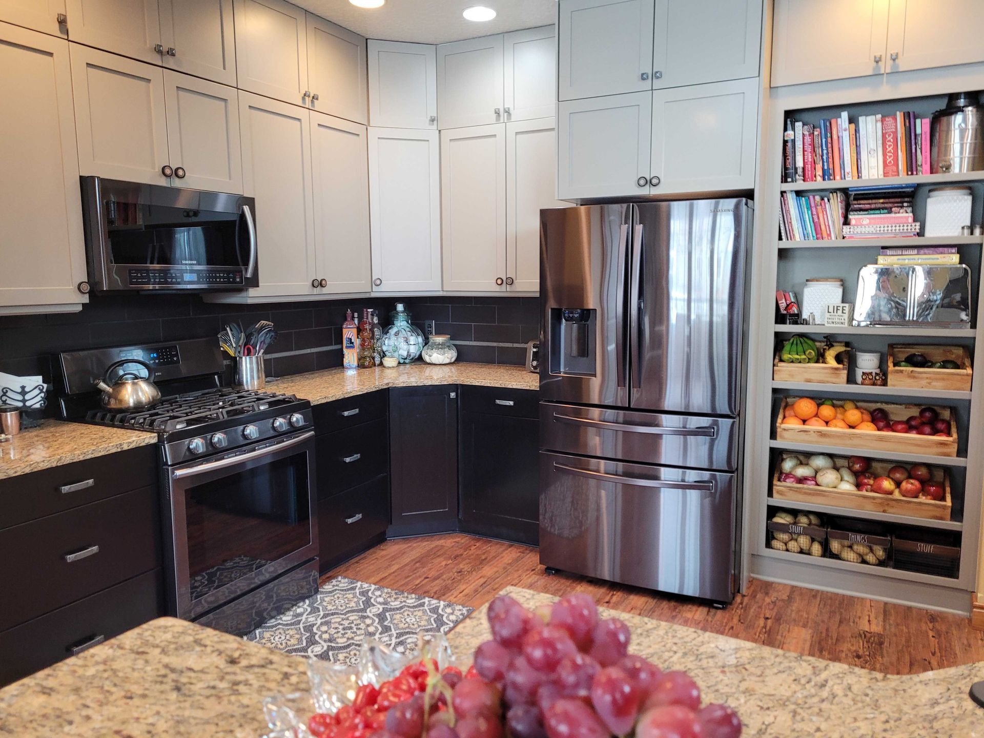 A modern kitchen featuring two-toned cabinetry, stainless steel appliances, and open shelving filled with food and books.