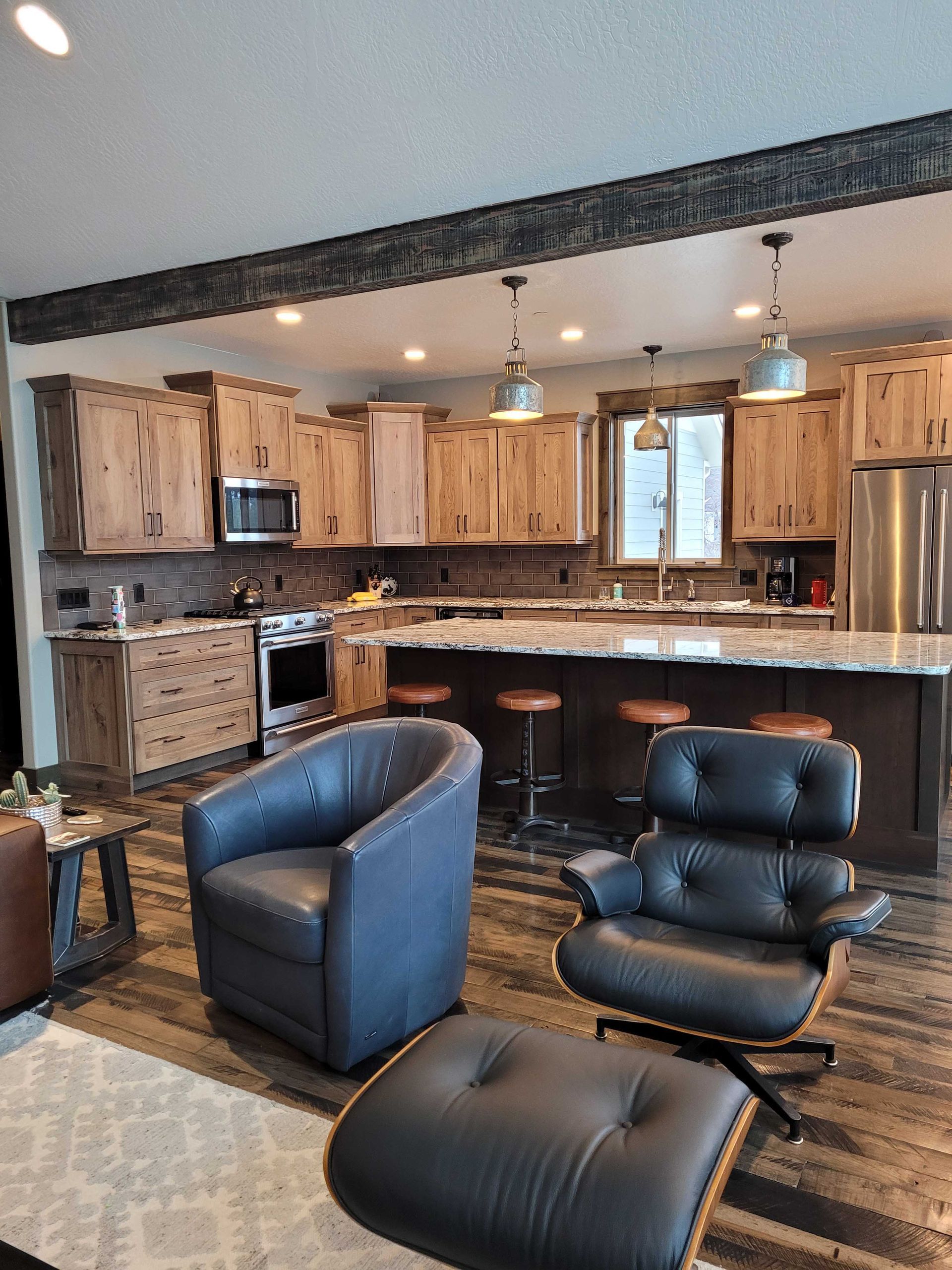 Modern kitchen with natural wood cabinets, a large island with three stools, and a comfortable seating area.