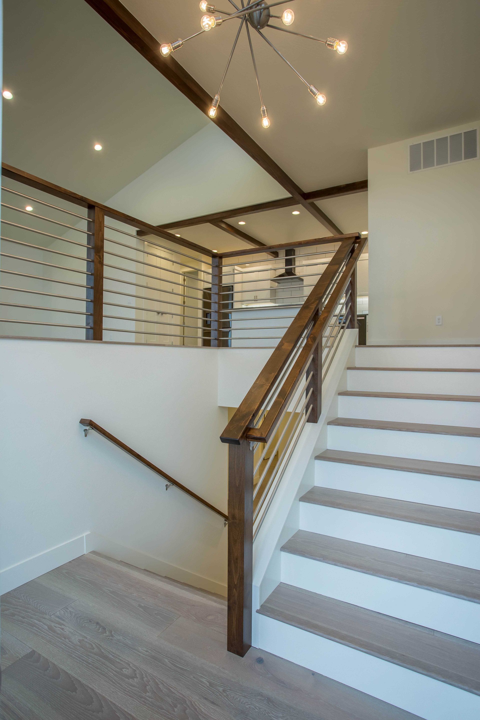 A staircase with wood-toned treads and railings ascends to a loft space featuring wood ceiling beams and a starburst light.