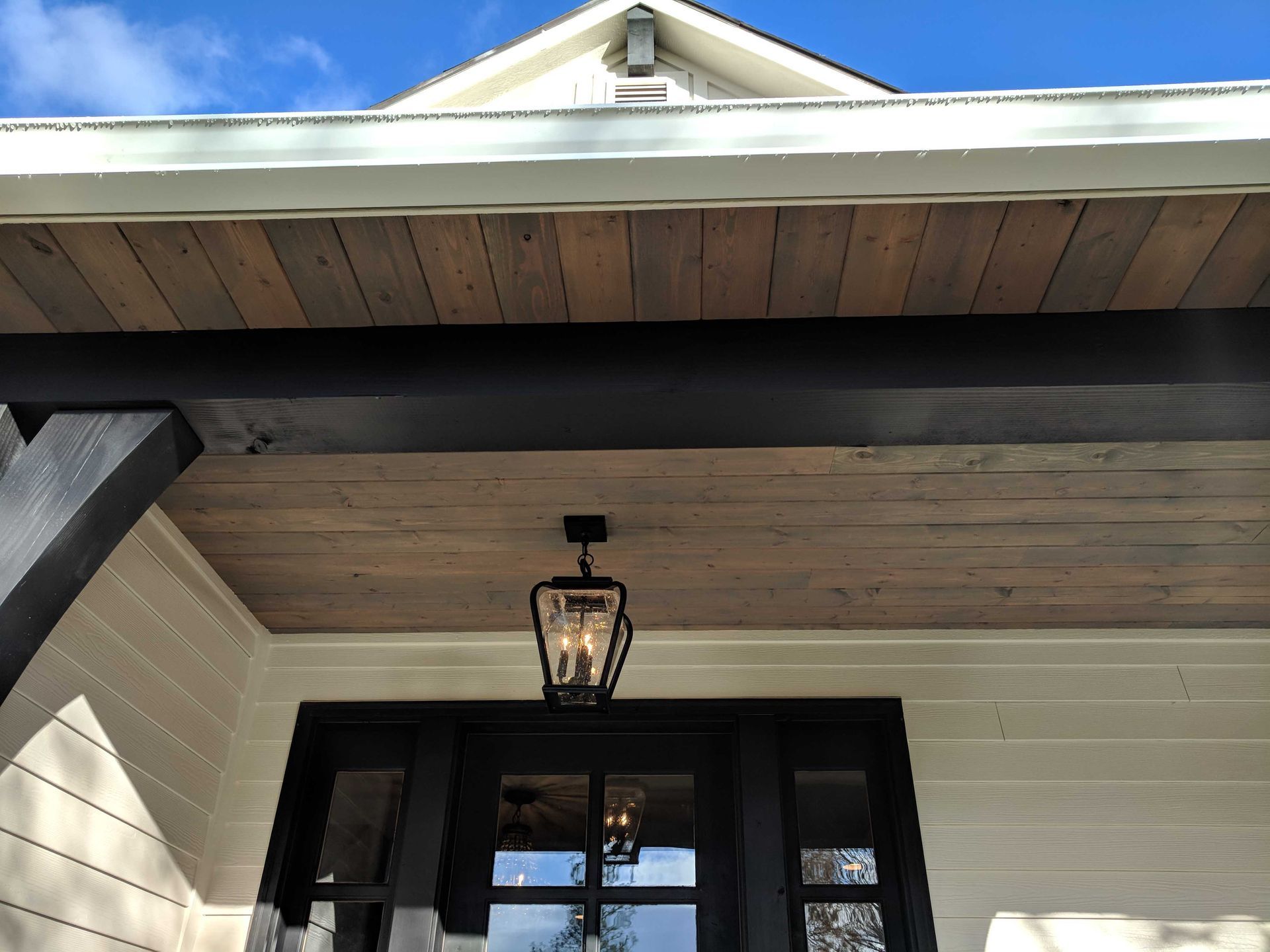 Front porch exterior with a lantern-style light fixture hanging from a wood-plank ceiling above a dark-framed glass door.