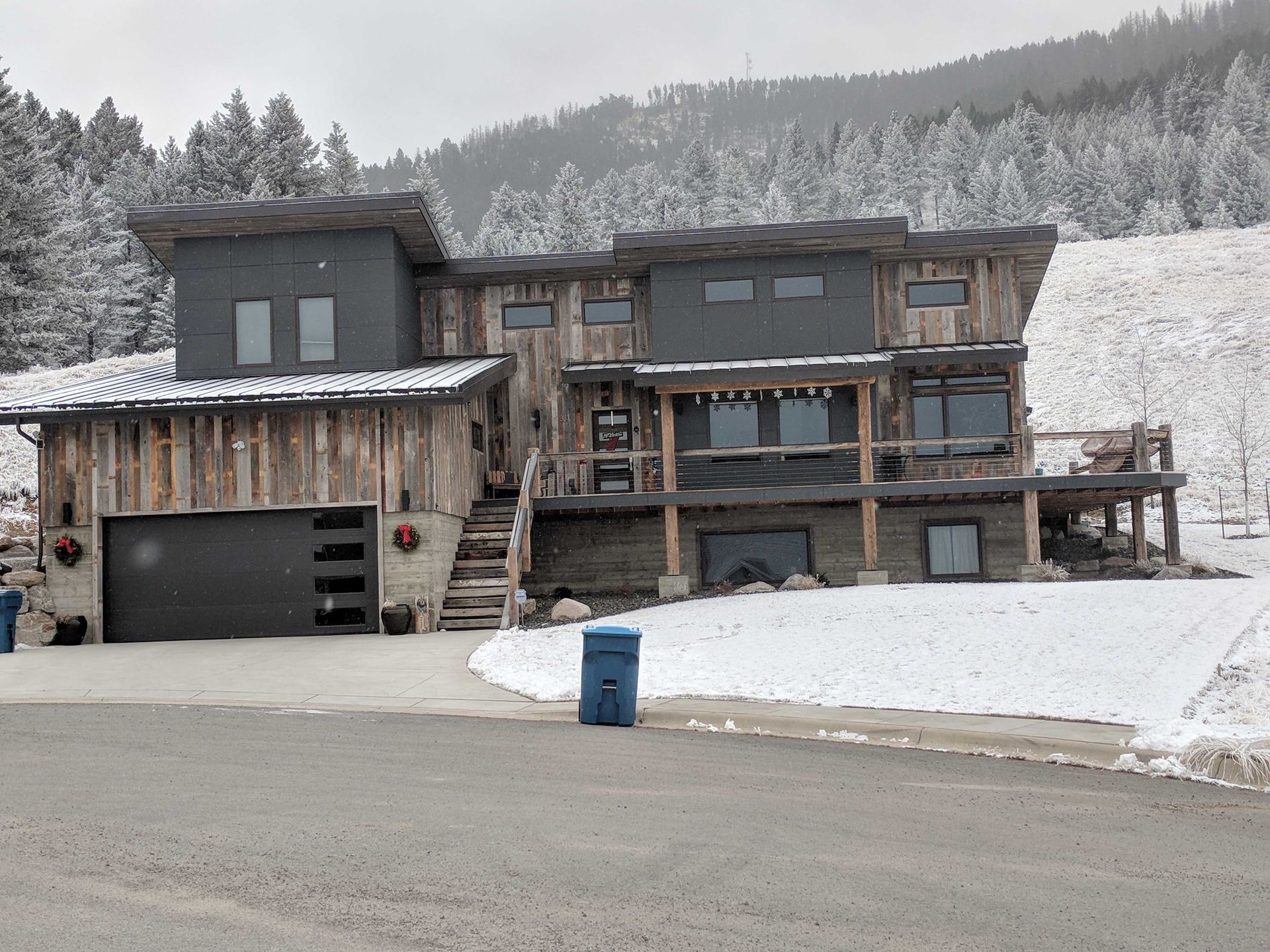 A two-story mountain home with dark gray panels and reclaimed wood siding, surrounded by a snowy landscape.